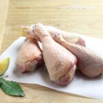 A platter of golden-brown baked chicken drumsticks, garnished with fresh herbs and served with a side of barbecue sauce and colorful vegetable sticks.