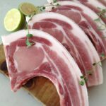 aw pork lion (pork tenderloin) displayed on a wooden cutting board, showcasing its lean, pink meat and smooth texture, surrounded by fresh herbs and spices for seasoning."