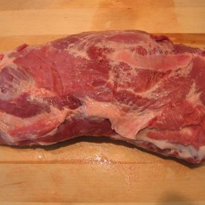 "A frozen boneless pork collar displayed on a cutting board, showcasing its marbled texture and rich color, with ice crystals visible on its surface."